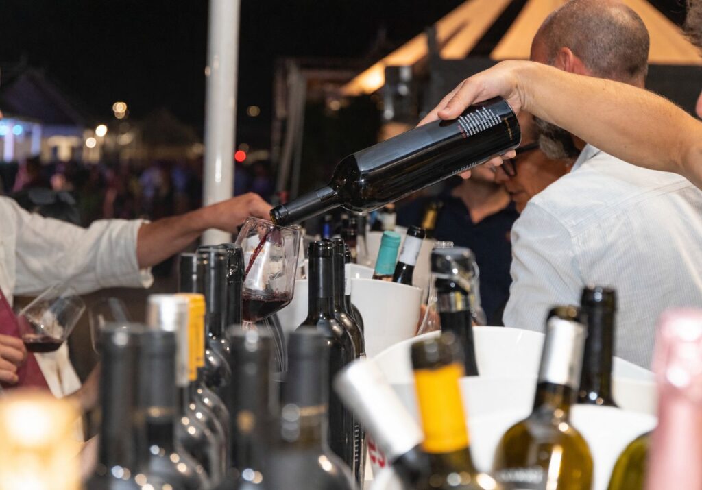 Banco d'assaggio di Vinòforum: mescita di vino rosso tra bottiglie al banco di degustazione serale
